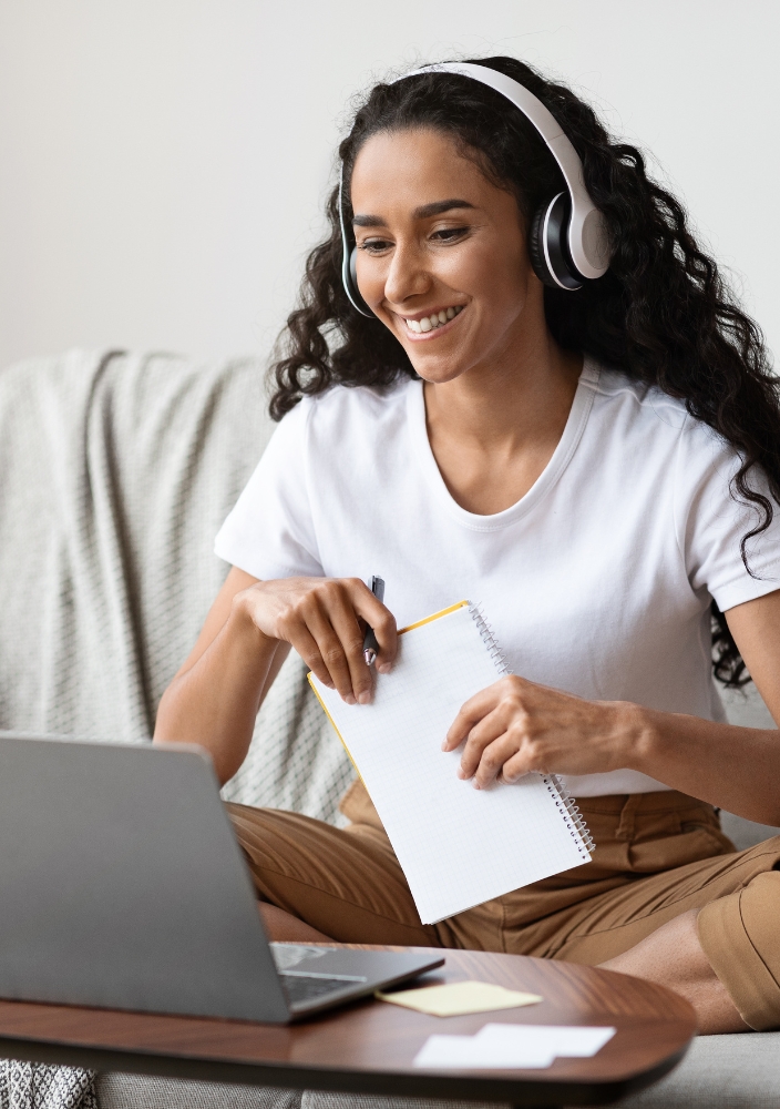 woman smiling at a computer, writing notes
