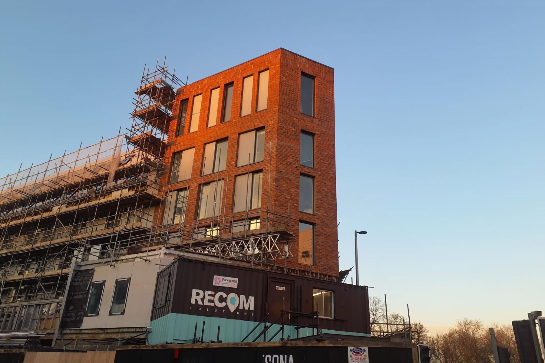 Image of a construction site with scaffolding on a building. Below is a storage container with the RECOM Solutions logo on it